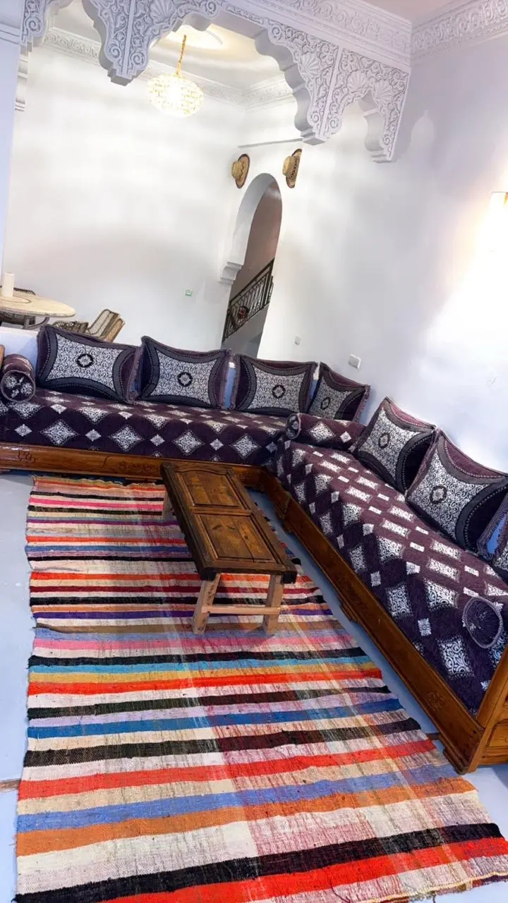 Salon marocain traditionnel avec banquettes brodées, table basse en bois et tapis berbère coloré